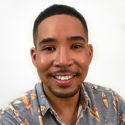 Headshot of De'Shan with short hair, a goatee, and wearing a hawaiian shirt.